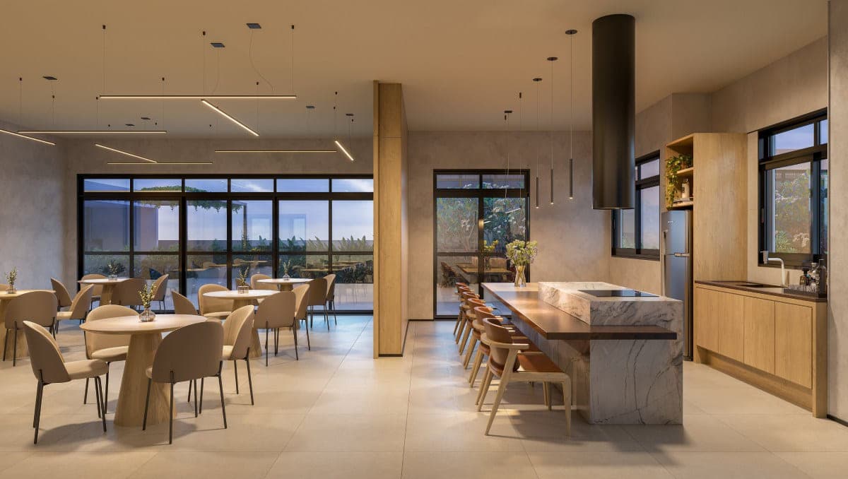 Salão gourmet com mesas redondas, bancada de pedra com banquetas altas e cozinha ao fundo
