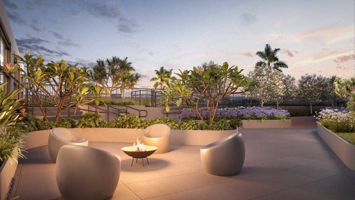 Terraço ao entardecer com poltronas em volta de uma lareira externa, cercado de paisagismo